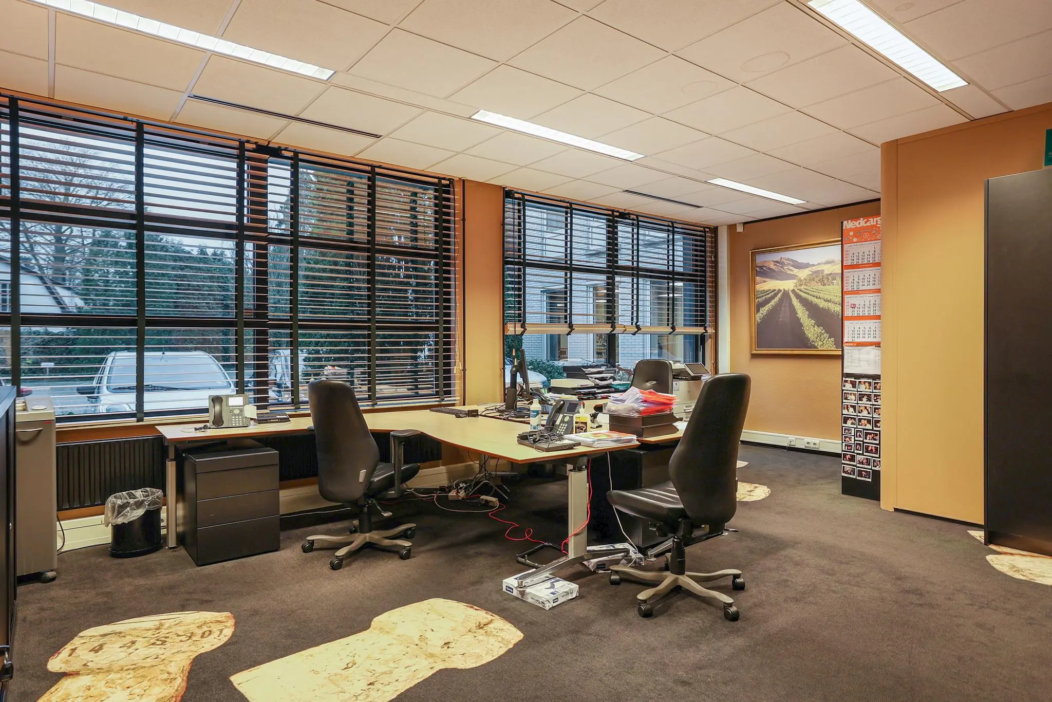 Kantoorruimte aan de Oude Utrechtseweg met bureaus, bureaustoelen en grote ramen met jaloezieën.